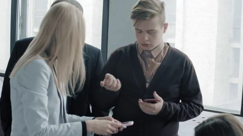 A group of colleagues are having fun talking to each other, holding smartphones Stock Footage 124329817