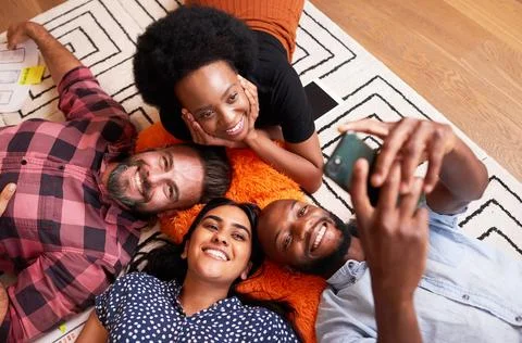 Group of colleagues at tech start up lie on the floor and take selfies fun break Foto stock