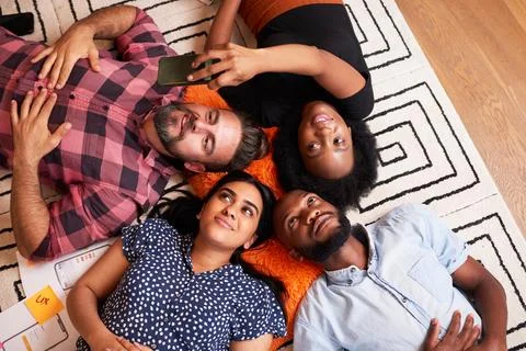 Group of colleagues at tech start up lie on the floor and take selfies fun break Stock Photos