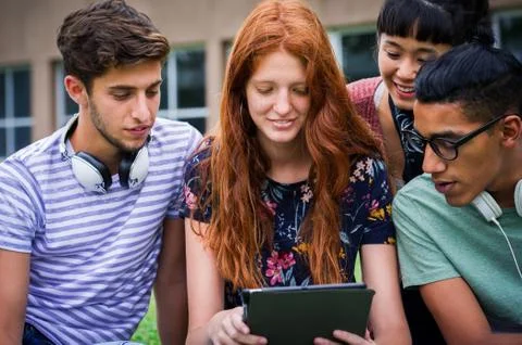 Group of college students looking at digital tablet together outdoors Stock Photos