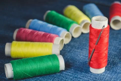 Group of colored thread spools and sewing needle on denim Stock Photos
