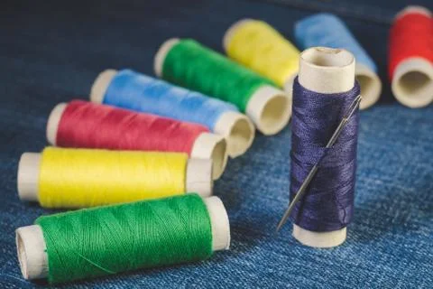 Group of colored thread spools and sewing needle on denim Stock Photos