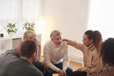 Group Consoling Man Speaking At Support Group Meeting For Mental Health Or Stockfoto's
