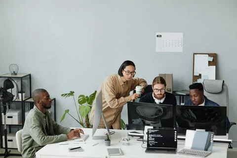 Group of contemporary program developers gathered in front of computer monitors Stock Photos
