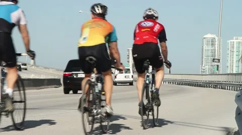 Group of cyclists go up bridge with city skyline in back ground Stock Footage 45946577