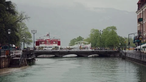Group of cyclists rides over canal bridge in Annecy in rainy day, France 库存影片 116786403