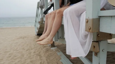 Group dangle feet over tower at beach Stock Footage