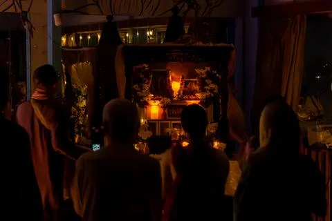Group of devotees facing ornate altar with photos candles and flowers under warm Stock Photos