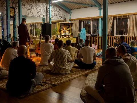 Group of devotees seated on rugs facing illuminated altar during evening kirtan Stock Photos