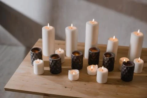 A group of different sized candles stands on a simple wooden table. Stock Photos