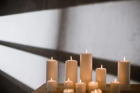 A group of different sized candles stands on a simple wooden table. Stock Photos