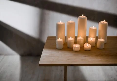 A group of different sized candles stands on a simple wooden table. Stock Photos