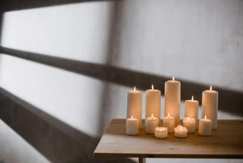 A group of different sized candles stands on a simple wooden table. Stock Photos