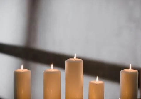 A group of different sized candles stands on a simple wooden table. Stock Photos