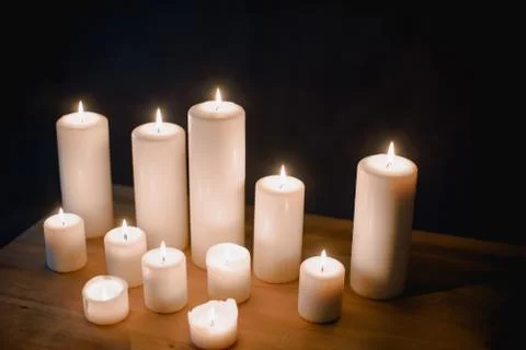 A group of different sized candles stands on a simple wooden table. Stock Photos