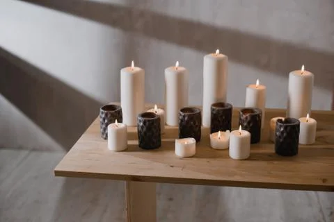 A group of different sized candles stands on a simple wooden table. Stock Photos