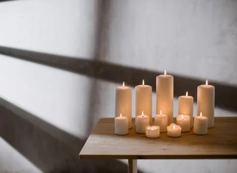 A group of different sized candles stands on a simple wooden table. Stock Photos