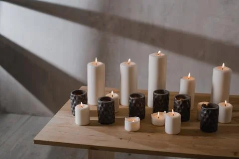 A group of different sized candles stands on a simple wooden table. Stock Photos