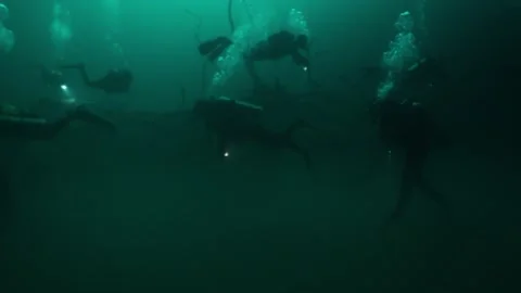 Group of divers with flashlights swimming in murky green water through an eerie Vídeos de archivo 332001853