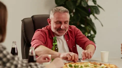 A group of diverse people sit at a table and prepare to eat pizza. The workers Stock Footage 243367410