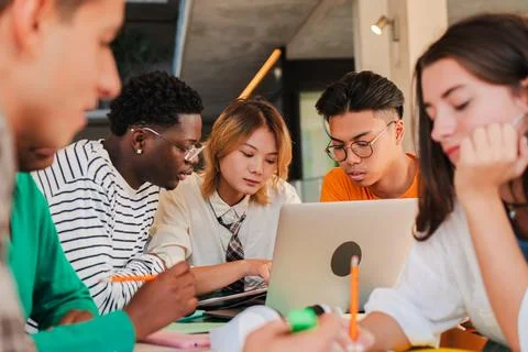 A group of diverse students is actively collaborating on a laptop in a modern Stock Photos