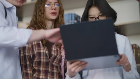 Group of diverse students working on laptop in library Видео 331866485