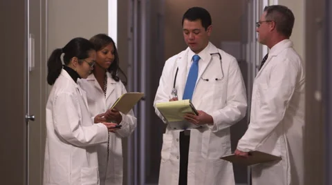 A group of doctors standing in the hallway talk and take notes and then look up Stock Footage 67343473