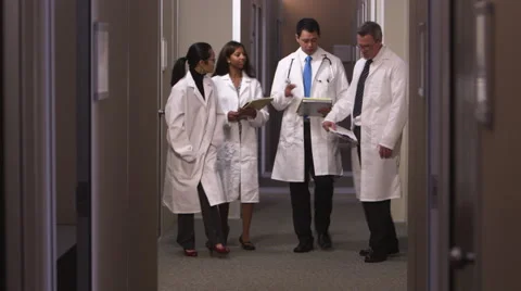A group of doctors talk as they walk down a hallway together Видео 67343440