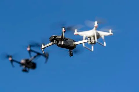 A Group Of Drones Fly Together Through The Air Against A Blue Sky Stock Photos