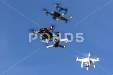 A Group Of Drones Fly Together Through The Air Against A Blue Sky Stock Photos