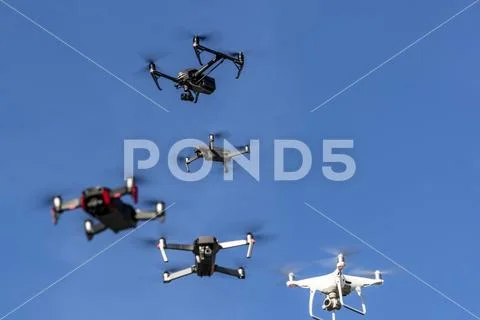 A Group Of Drones Fly Together Through The Air Against A Blue Sky Stock Photos