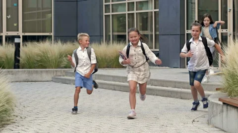 Group of elementary school students joyfully run out of the school building. End Video stock 212898725