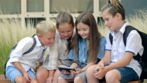 Group of elementary school students sit on a bench in the schoolyard. Children Stock Footage 205204277