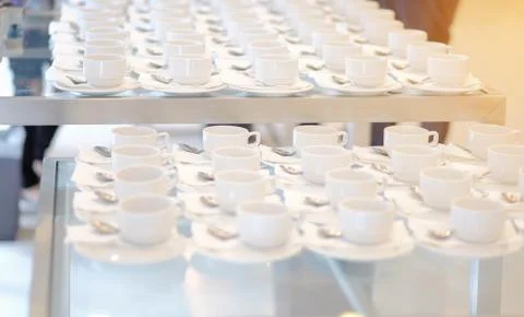 Group of empty Many rows of white ceramic coffee or tea cups and spoons on gl Stock Photos