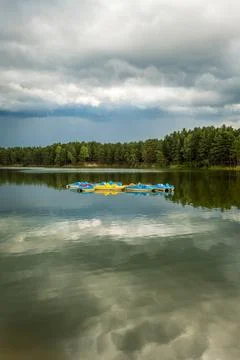 A group of empty yellow and blue pedal boats in the middle of a lake. Stock Photos