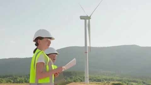 A group of engineers is examining wind turbine blueprints outdoors, donning Stock Footage 285841805