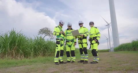 Group of engineers in reflective uniform discussing data at wind turbine field, Stock Footage 337165025