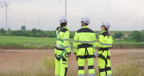 Group of engineers in safety gear observing wind turbines from distance, Stock Footage 321791167