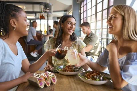 Group Of Female Friends Meeting Up In Restaurant Eating Food And Doing Cheers Stock Photos