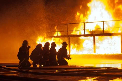 Group of firefighters spraying down burning structure during firefighting e.. Stock Photos