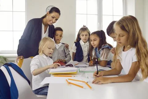 Group of first graders learn to write and read under guidance of friendly female Stock Photos