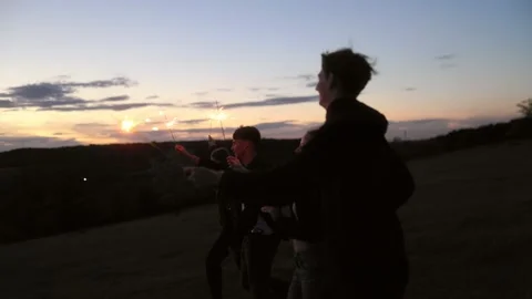 Group of five energetic teens running and dancing with sparklers at dusk. Video stock 336249740