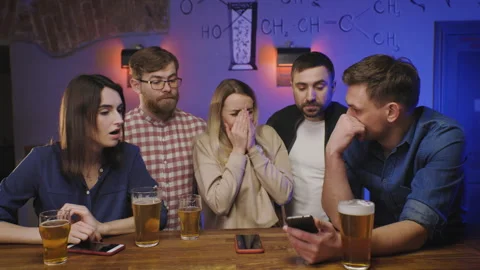 Group of five friends sit together at bar, intensely focused on a smartphone Stock Footage 286821419