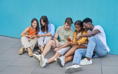 Group of five multiethnic student friends sitting on the ground at school using Stock Photos