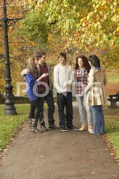 Group of five teenage friends chatting in autumn park Stock Photos