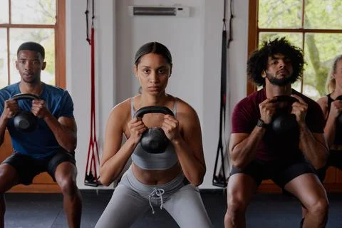 Group of focused multiracial young adults doing kettlebell squats at the gym Stock Photos