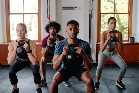 Group of focused young adults doing kettlebell squats at the gym Stock Photos