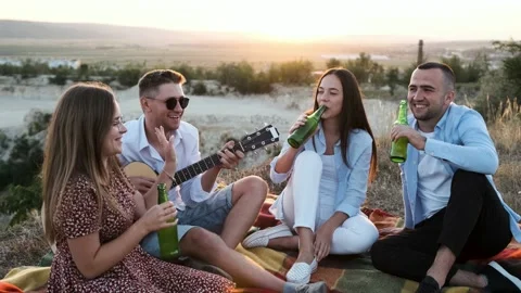 Group of four friends having fun at the summer picnic and drink a bottle of beer Stock Footage 138740880