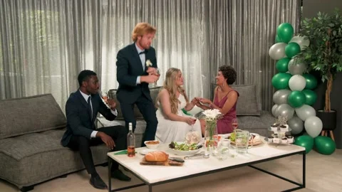 Group of four sitting on sofa celebrating wedding with confetti falling, man Stock Footage 334728569