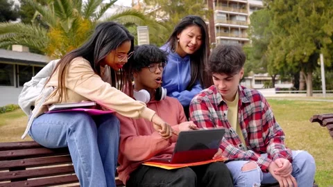 Group of four students smiling and have fun outdoors using a laptop. Teenage Stock Footage 245114109